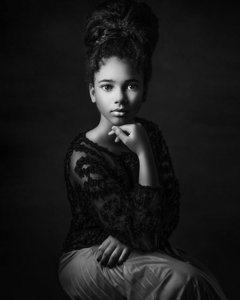 black and white portrait of Afro American girl sitting on a chair created with Rembrandt studio light set up